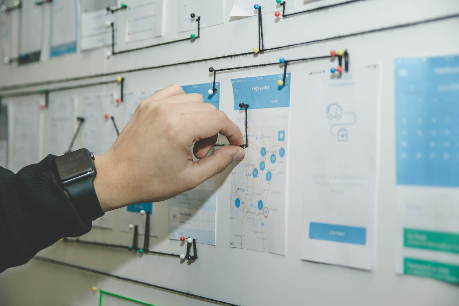 Screens pinned to a wall and joined with string, a workflow mapped by hand